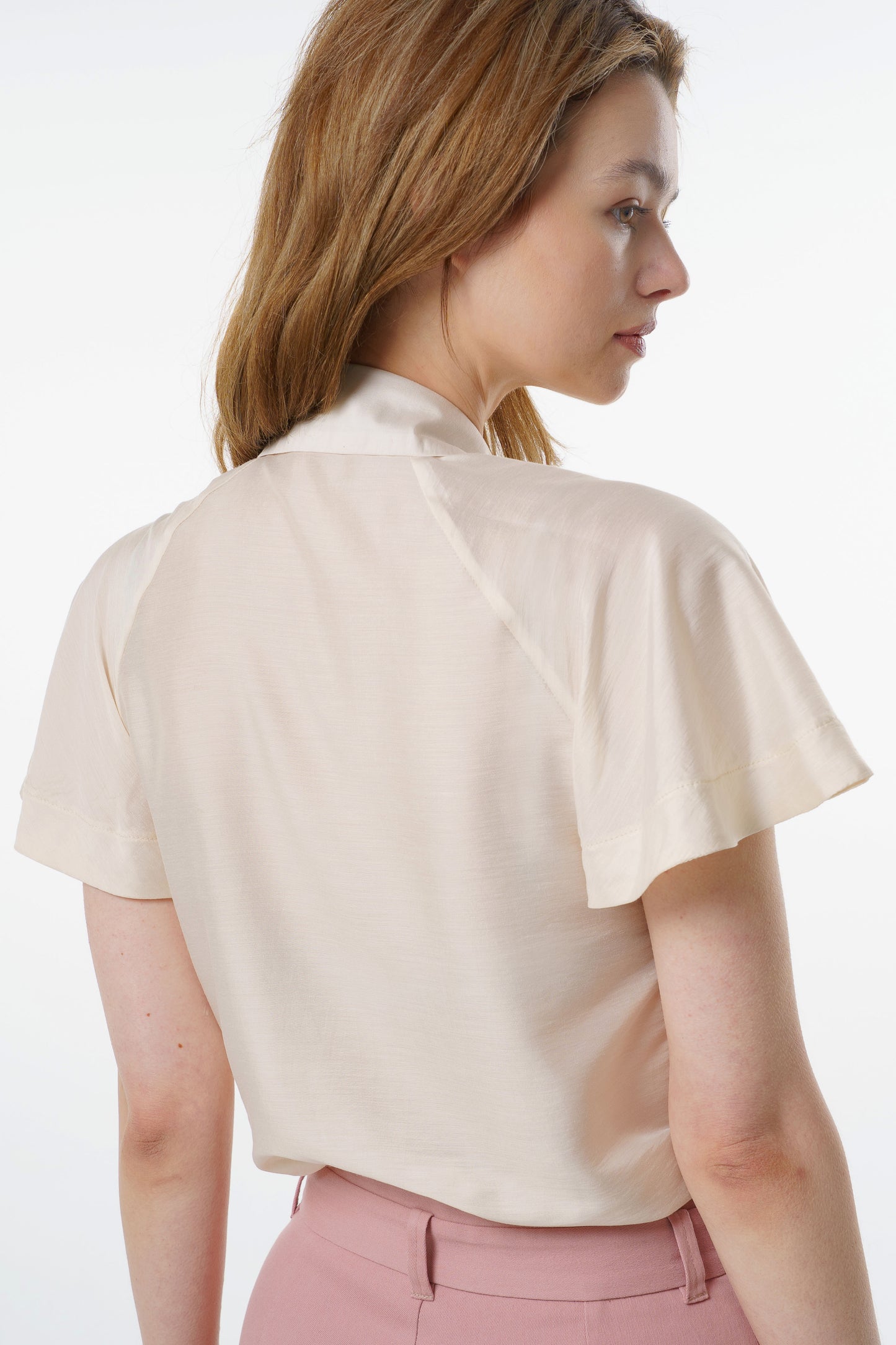 Ivory short‑sleeve silk–viscose blouse with flared raglan sleeves and relaxed back drape, worn by a model with high‑waisted rose‑dust trousers, back studio view.
