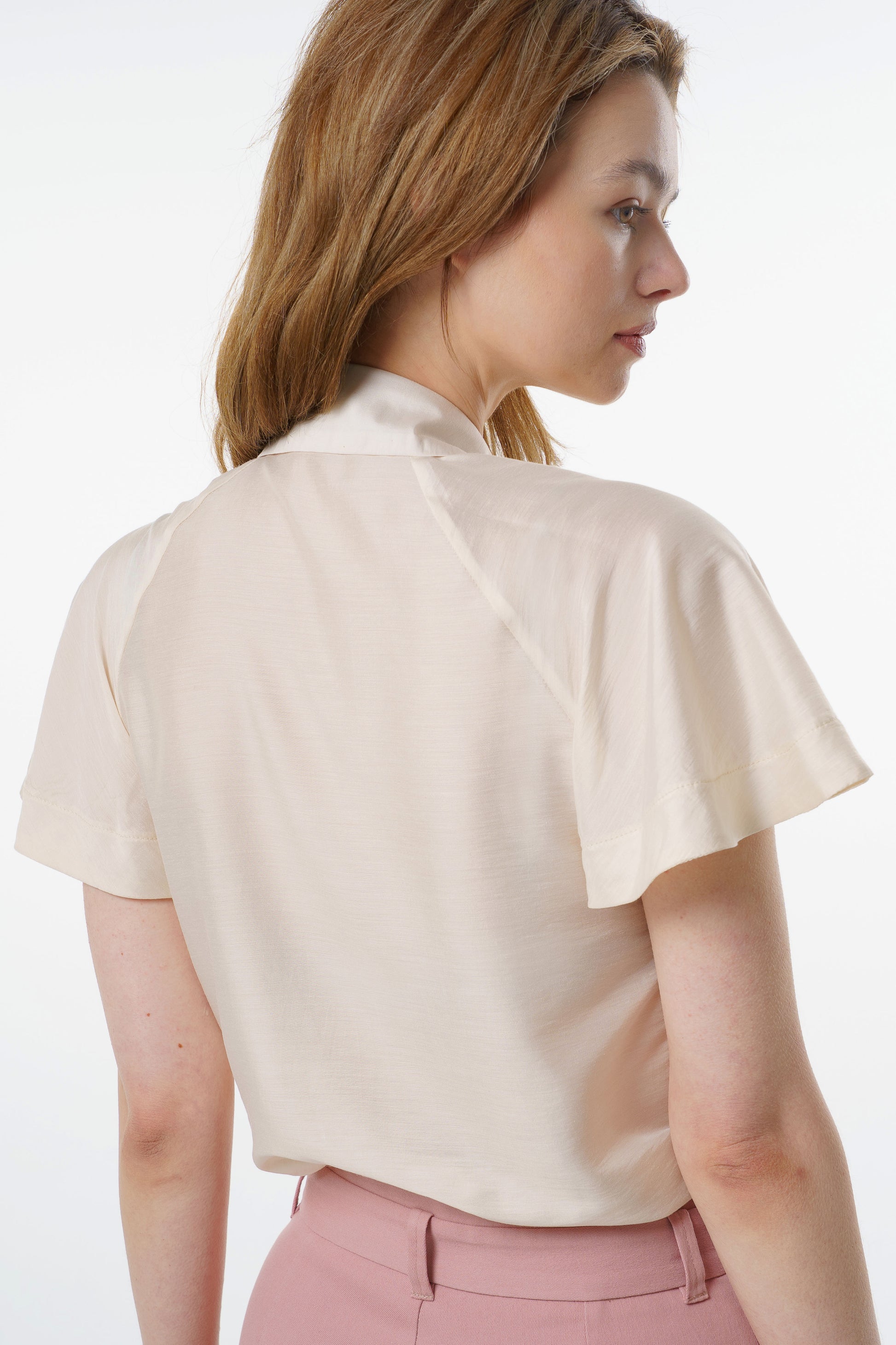 Ivory short‑sleeve silk–viscose blouse with flared raglan sleeves and relaxed back drape, worn by a model with high‑waisted rose‑dust trousers, back studio view.