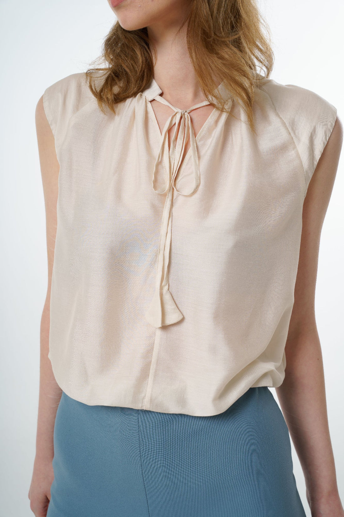 Close‑up of ivory sleeveless silk–viscose blouse showing front tie detail and soft sheen, worn by a model.