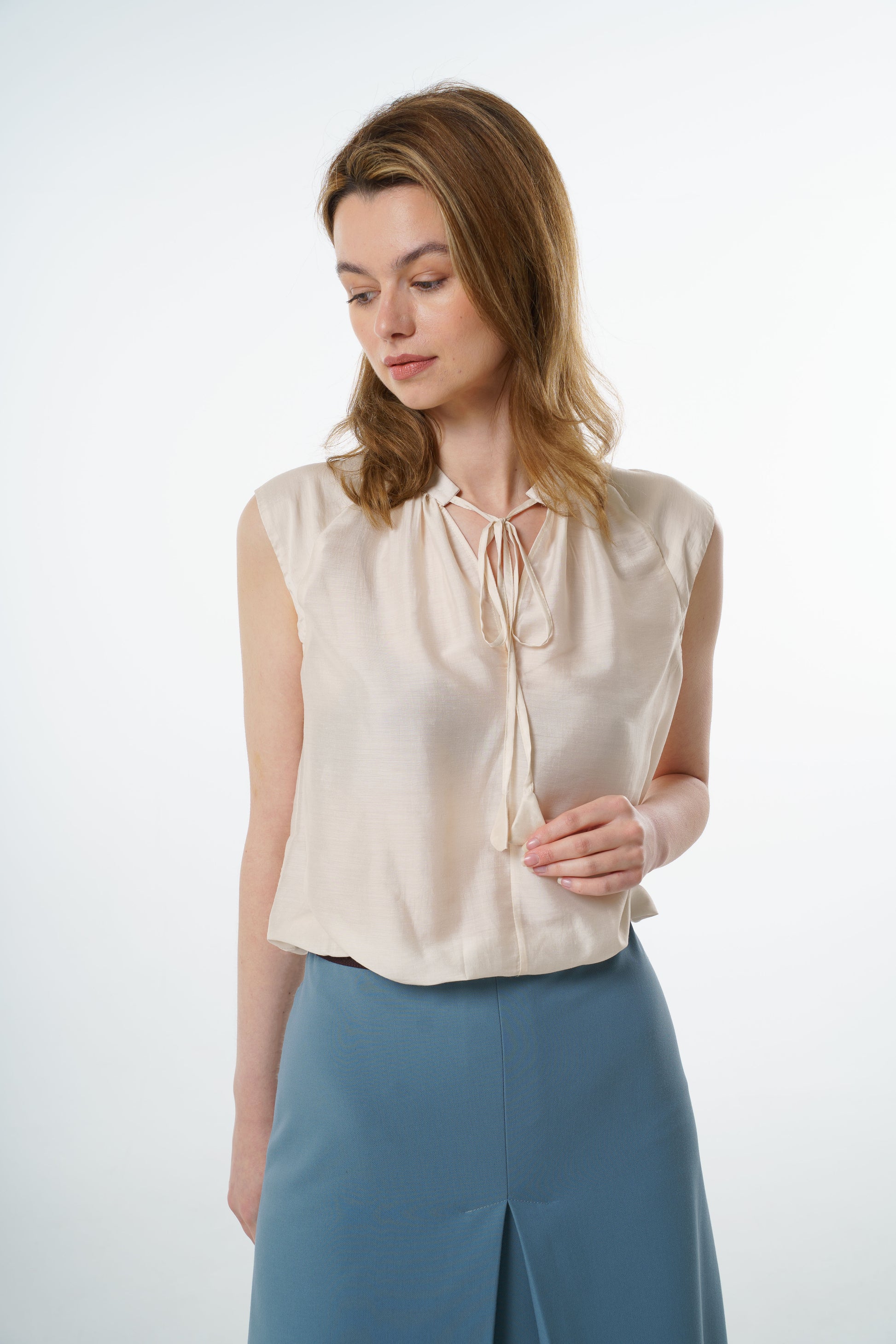 Ivory sleeveless silk–viscose blouse with front tie and relaxed fit, worn by a model with a high‑waisted blue skirt, front studio view.