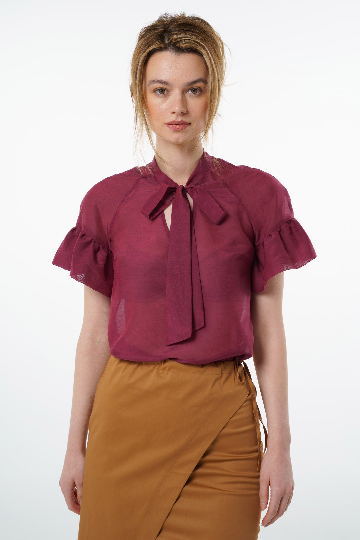 Burgundy viscose–silk raglan‑sleeve blouse with neck tie and soft ruffled cuffs, worn by a model with a high‑waisted mustard wrap skirt, front studio view.