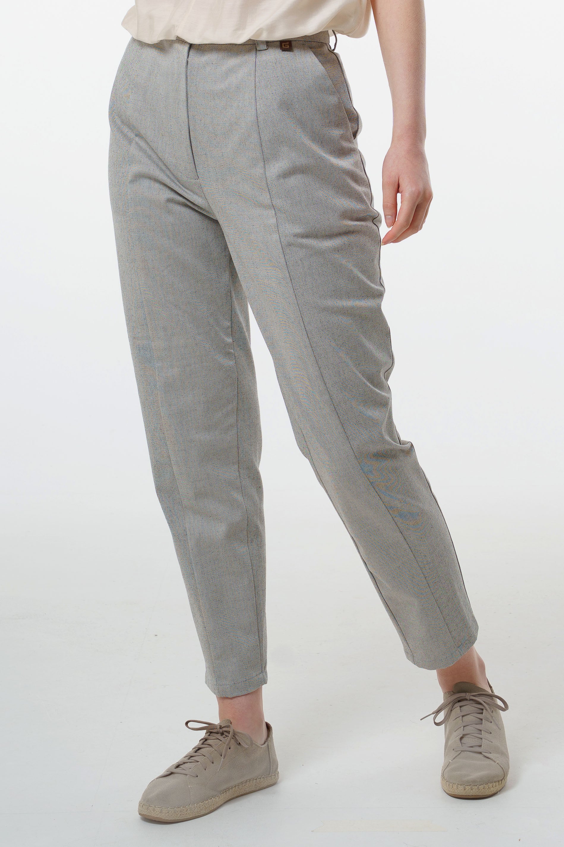 Close‑up of light grey tapered carrot‑leg trousers in a cotton blend showing front seam and tapered hem, worn by a model.