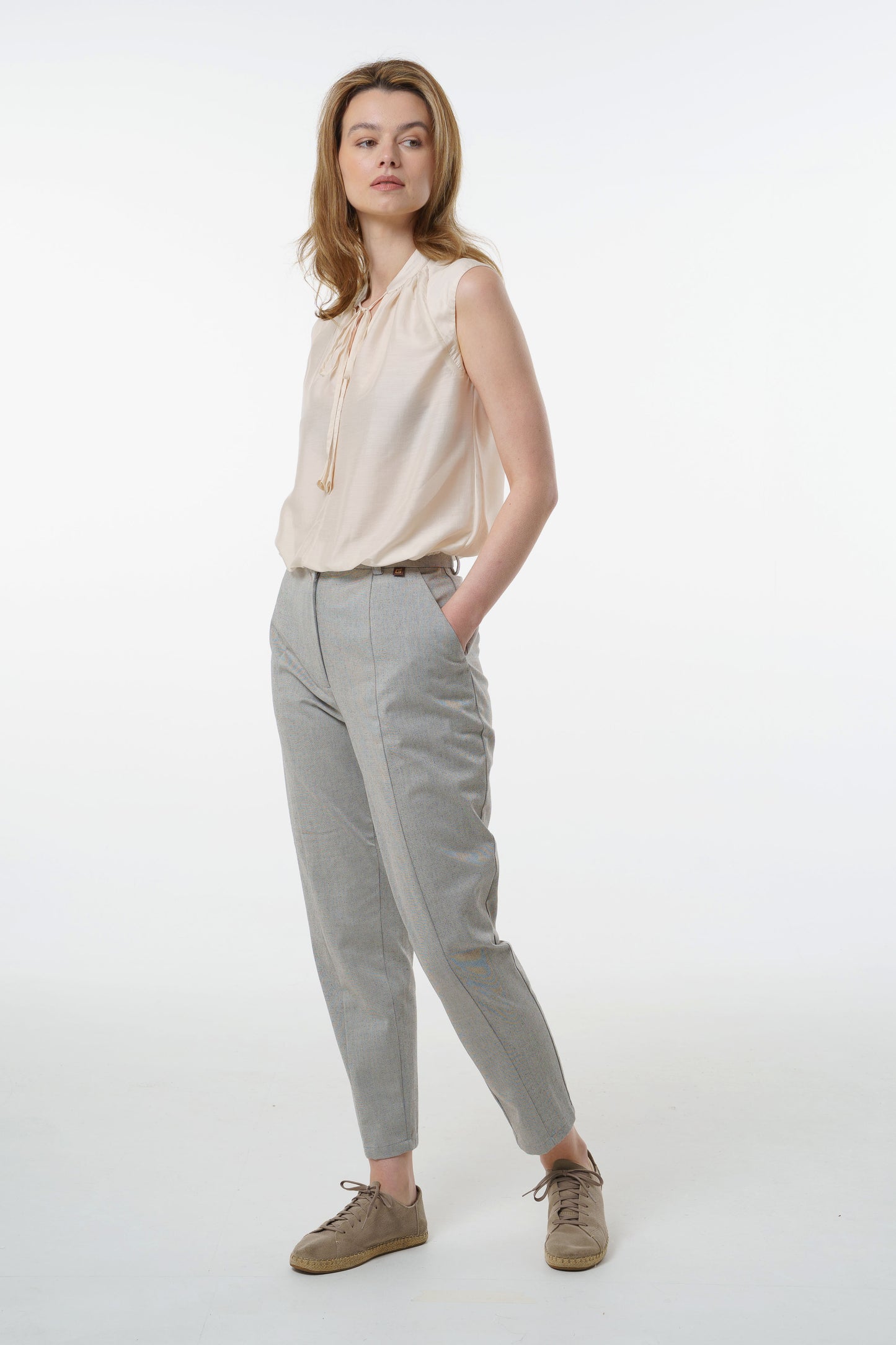 Light grey tapered carrot‑leg trousers in a cotton blend with structured front seam and tailored rise, worn by a model, angled front studio view.