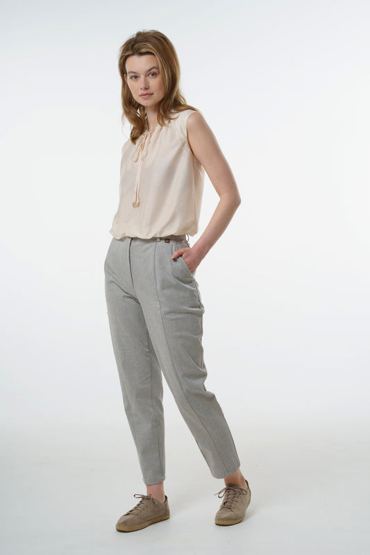 Light grey tapered carrot‑leg trousers in a cotton blend with front seam detailing and high‑waisted fit, worn by a model with a sleeveless blouse, front studio view.