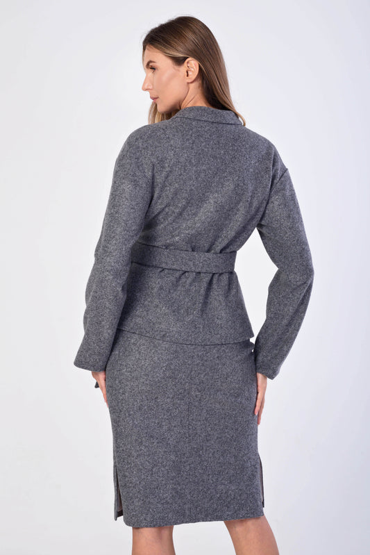 A woman shown from the back wearing a gray belted long-sleeve jacket over a matching gray pencil skirt, photographed against a plain light gray studio background.