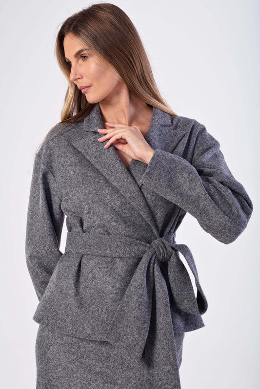 A woman wearing a gray wool wrap jacketwith a matching tie belt, photographed against a plain light gray studio background.