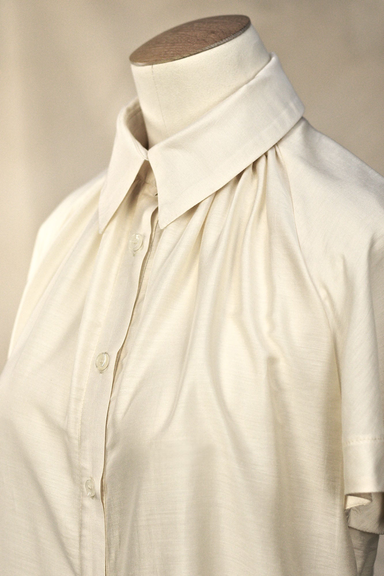 Close-up angled view of Ivory short‑sleeve silk–viscose blouse with flared raglan sleeves on  a mannequin, showing the classic shirt collar and soft gathering at neck line.