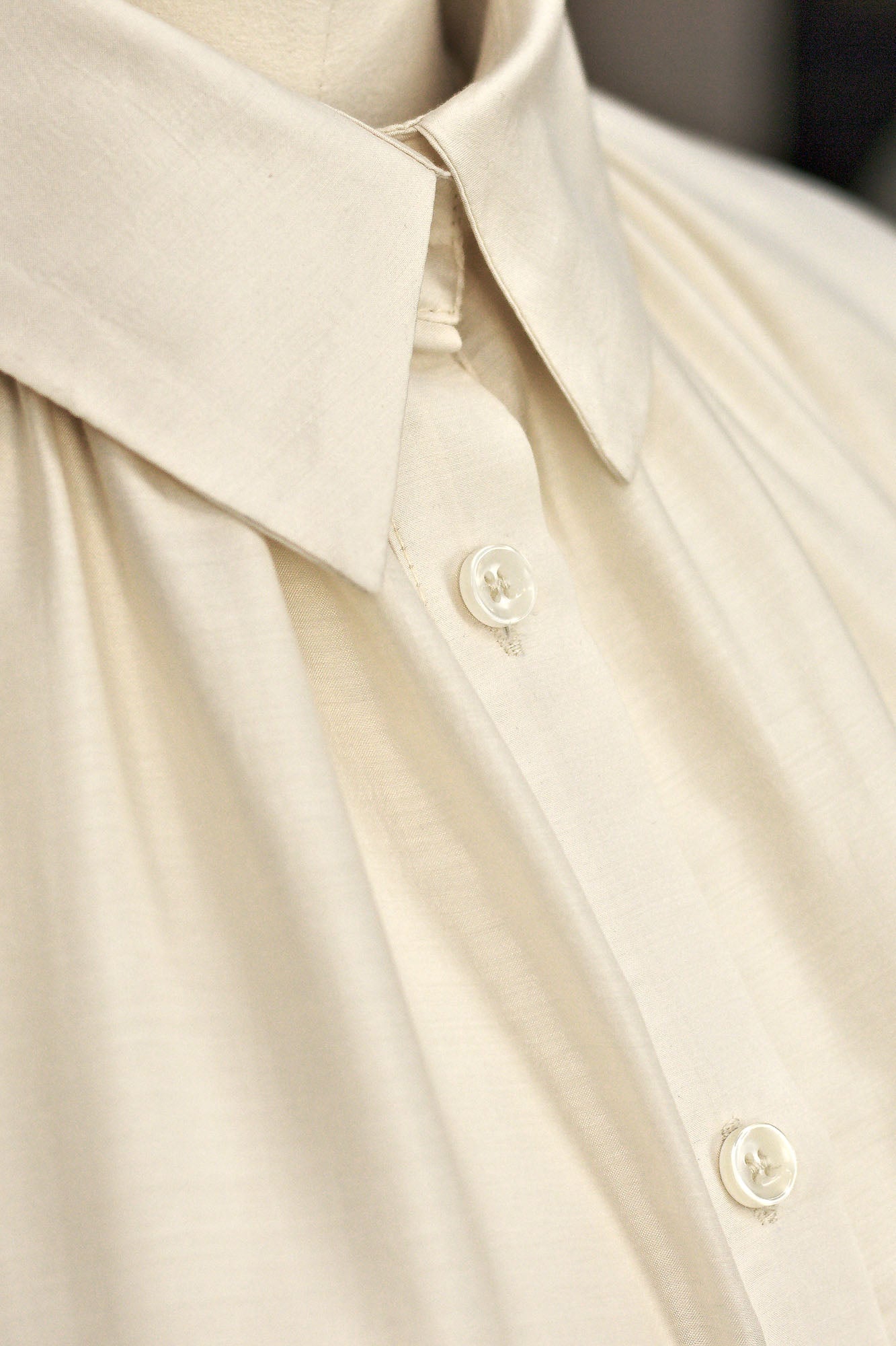 Macro view of Ivory short‑sleeve silk–viscose blouse on a mannequin, showing the classic shirt collar and button down fastening.