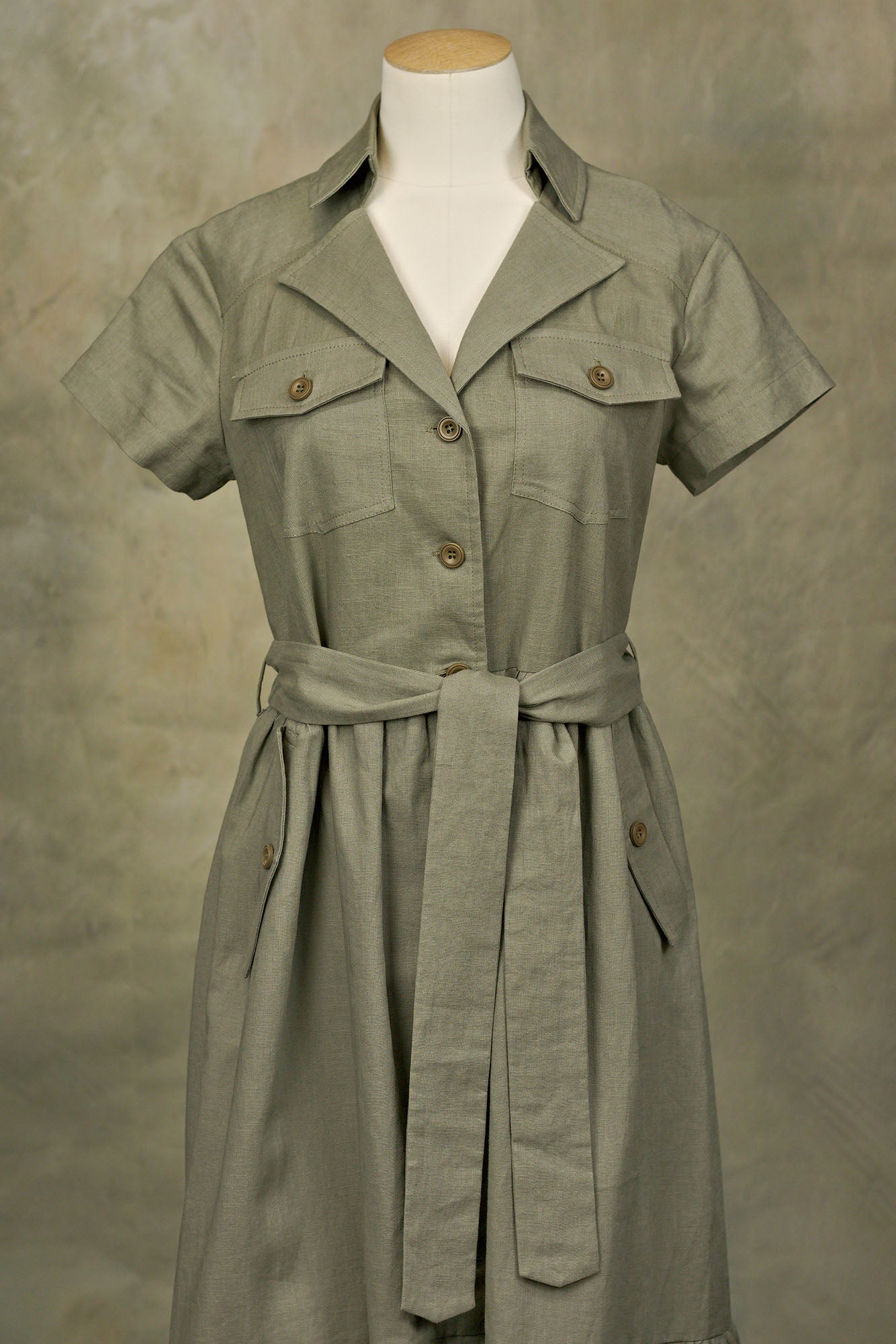 Olive green linen button‑down shirt-dress with collared neckline, chest pockets, and belted waist, on a mannequin, front studio shot.