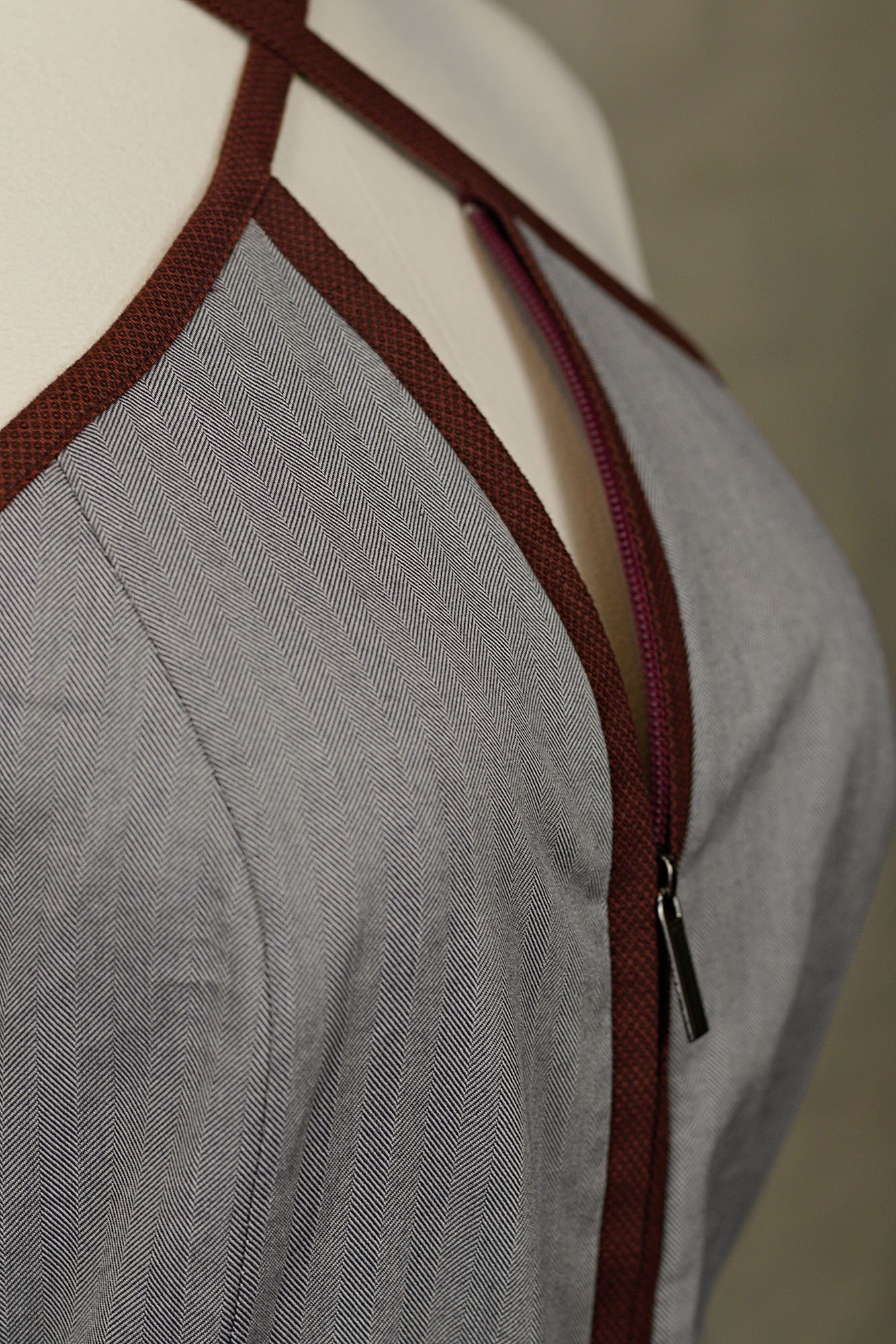 3/4 macro view‑up of grey jumpsuit with wine‑red trim and zip‑front closure, on a mannequin.