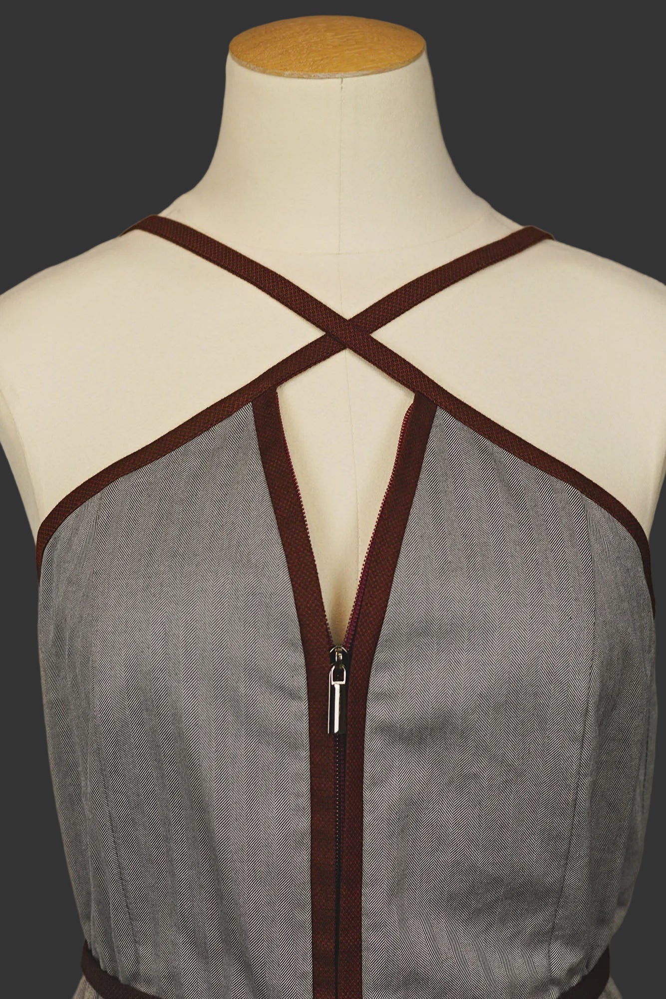 Close‑up of grey jumpsuit with wine‑red trim, zip‑front closure, and tied belt, on a mannequin.