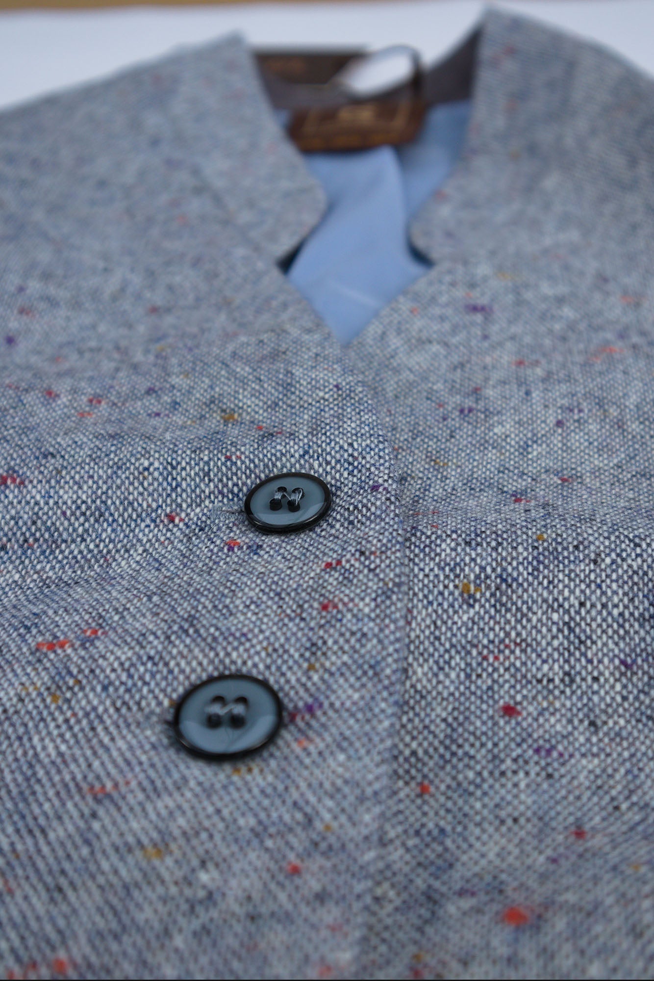 Macro view of a light blue wool tailored midi dress with  subtle speckled texture showing front button factening, flat studio view.