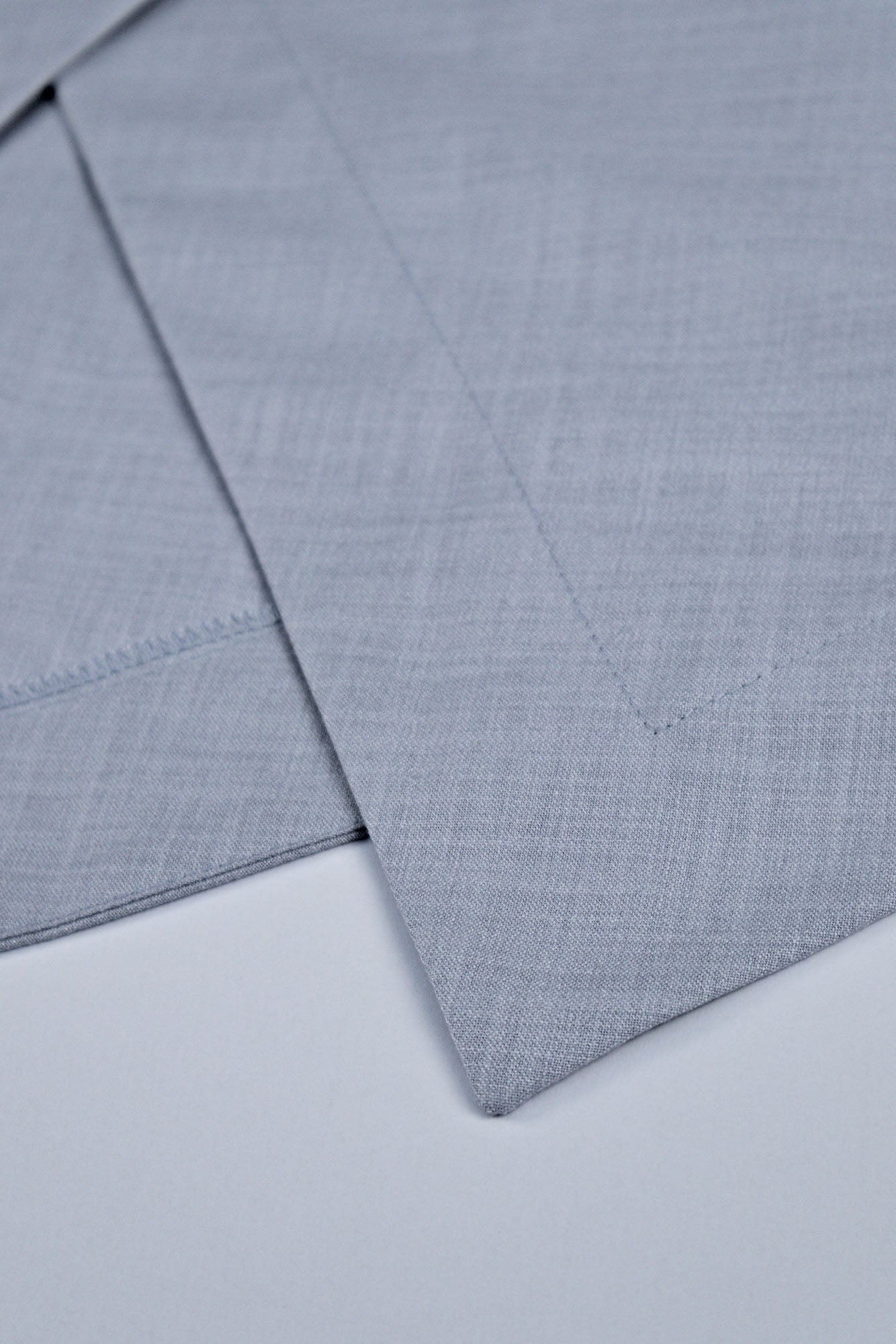 Macro view of pale blue midi dress in textured woven fabric showing hem details and seams.