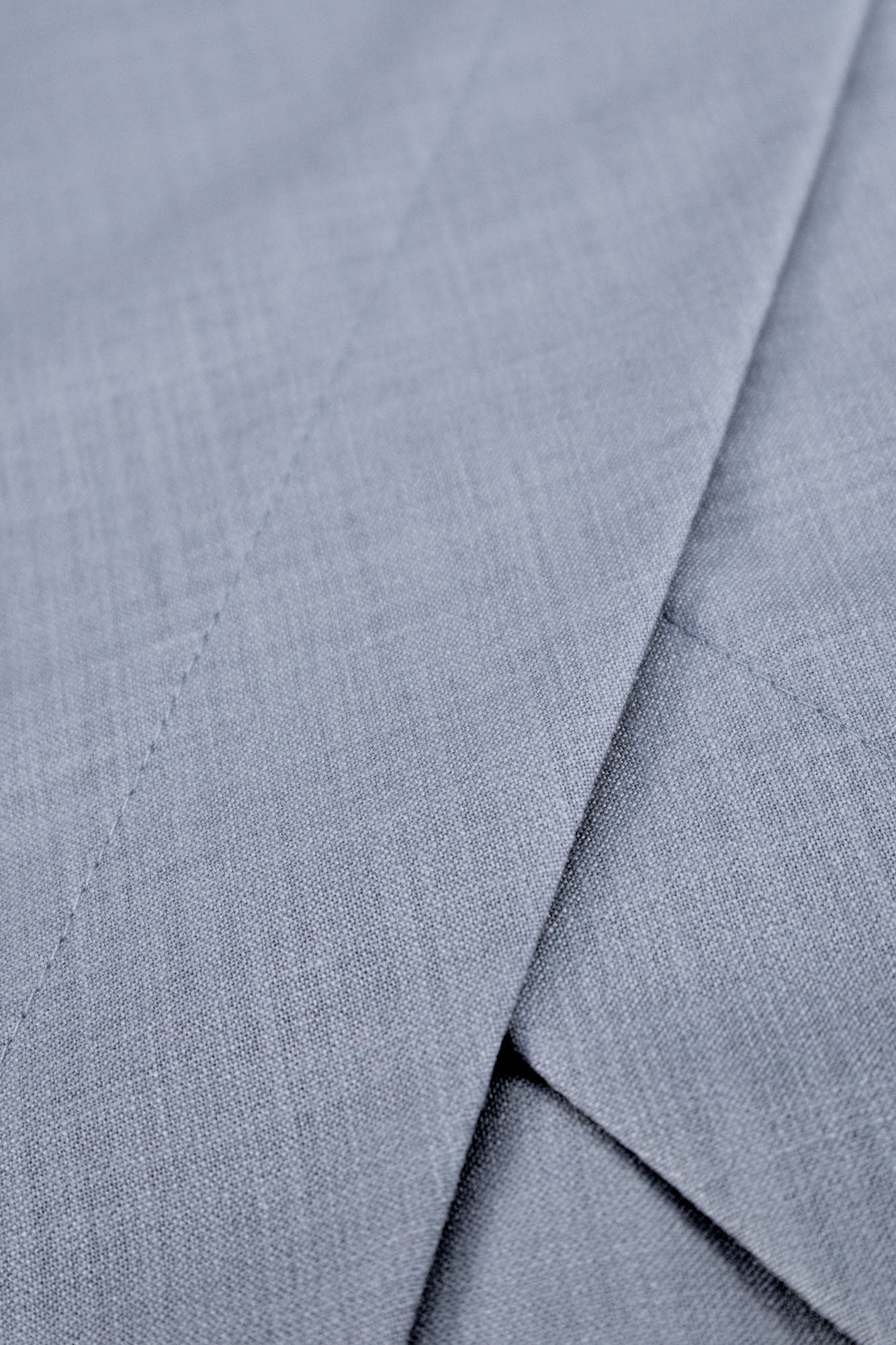 Macro view of pale blue midi dress in textured woven fabric showing wrap skirt details and seams.