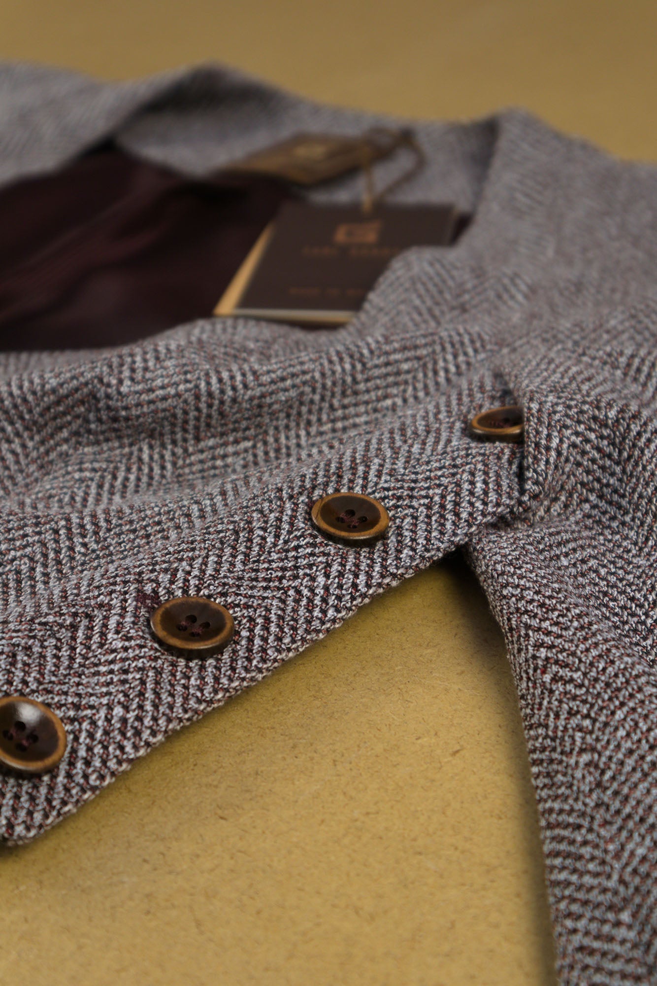 Macro view of a cropped woven top with herringbone texture, and wooden side‑button fastening, flat laying angled front view. 