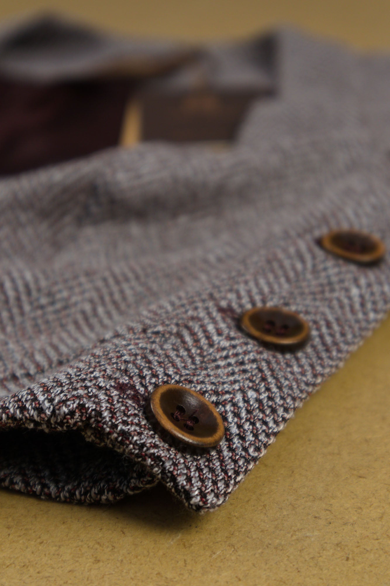Macro view of a cropped woven top with herringbone texture showing side‑button fastening, flat laying angled front view. 