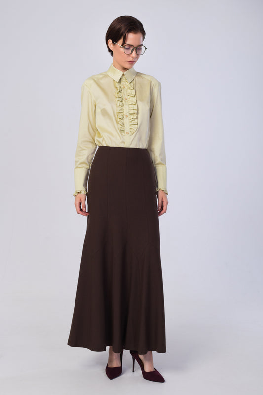 A model wearing a pale yellow long-sleeve blouse with a ruffled front and a dark brown high-waisted maxi skirt, paired with dark burgundy heels, against a light gray studio background.