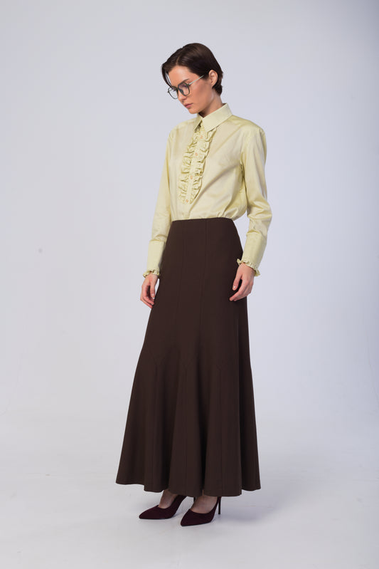 A woman modeling a light yellow long-sleeve blouse with a ruffled front and a dark brown high-waisted maxi skirt, paired with dark brown heels, against a light gray studio background.