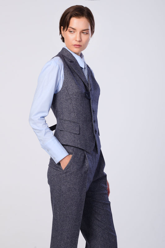 A model wearing a slate-blue tweed waistcoat and matching trousers over a light blue dress shirt, posed against a light gray studio background.