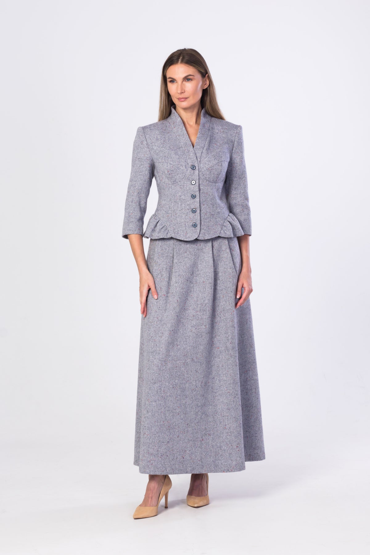 A woman modeling a matching light blue-grey two-piece suit consisting of a cropped jacket with three-quarter sleeves and a high-waisted maxi skirt, photographed against a plain light gray studio background.