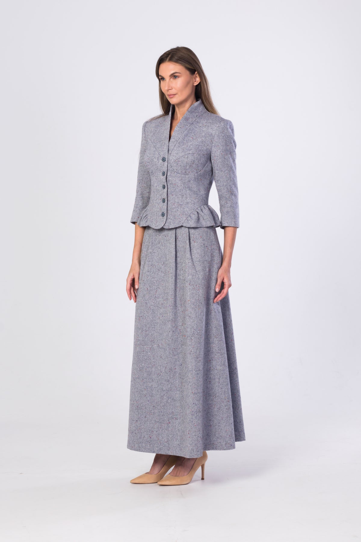 A woman modeling a matching light blue-grey two-piece outfit consisting of a cropped button-front jacket with three-quarter sleeves and a high-waisted maxi skirt, paired with beige heels, against a light gray studio background.