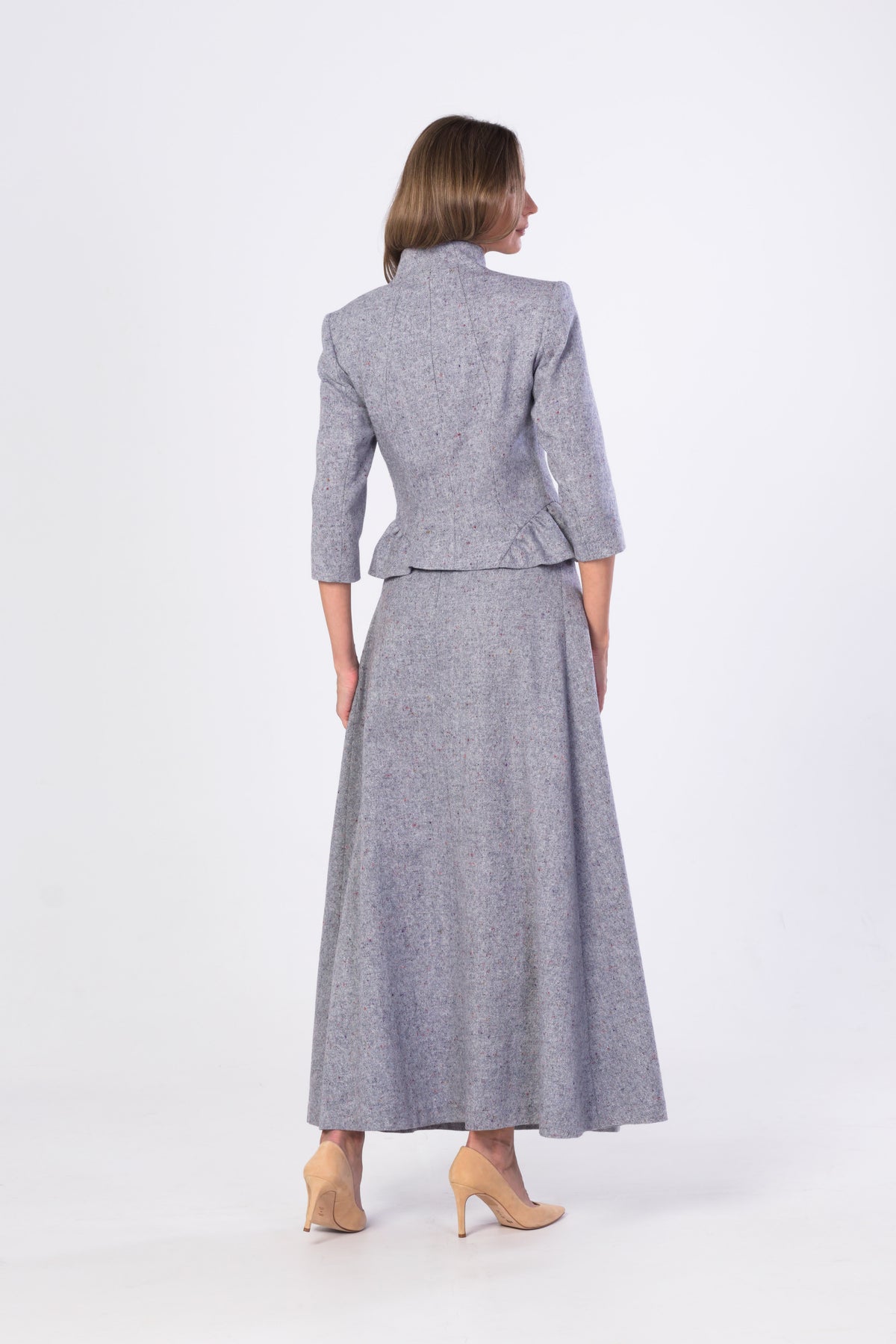 A woman shown from the back wearing a matching light blur-grey tweed blazer and long skirt set, paired with beige heels, against a plain white studio background.