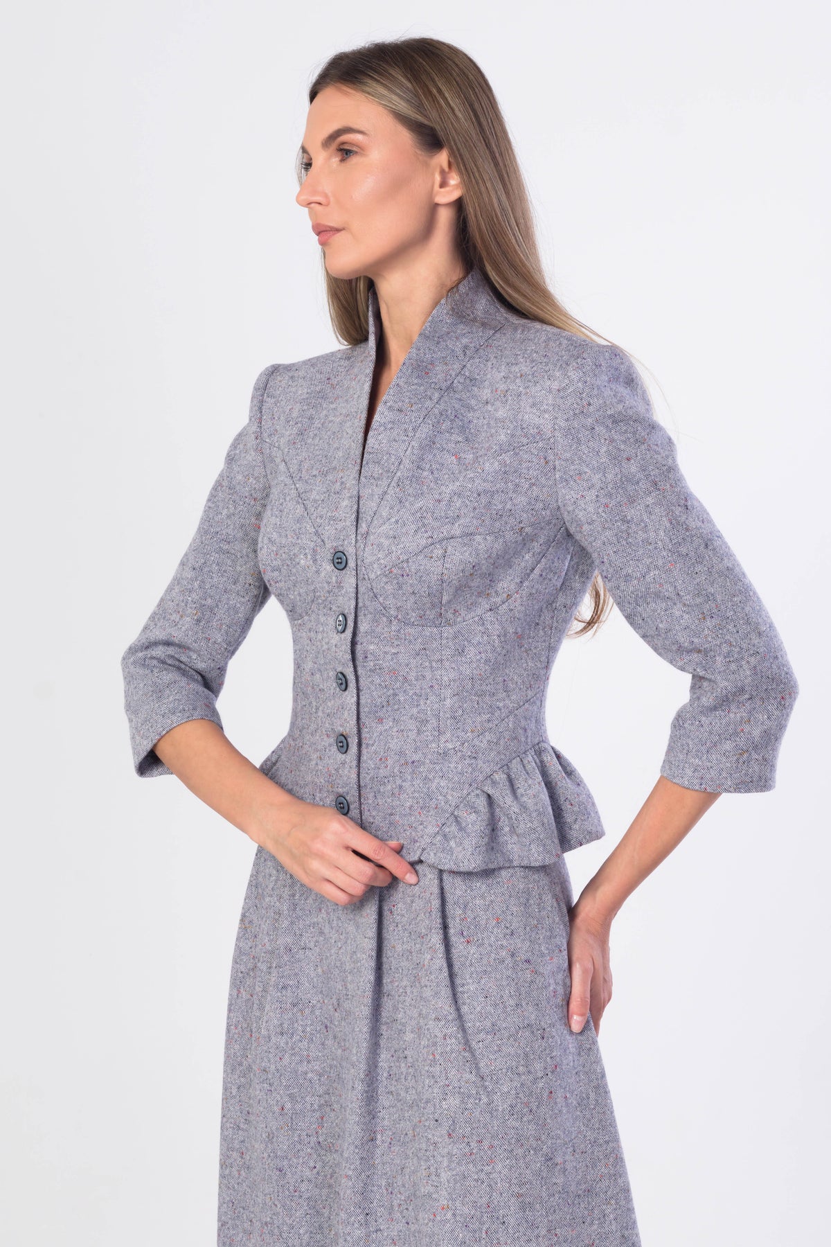A woman modeling a lght blue-grey tweed peplum jacket and matching skirt set against a plain white studio background.