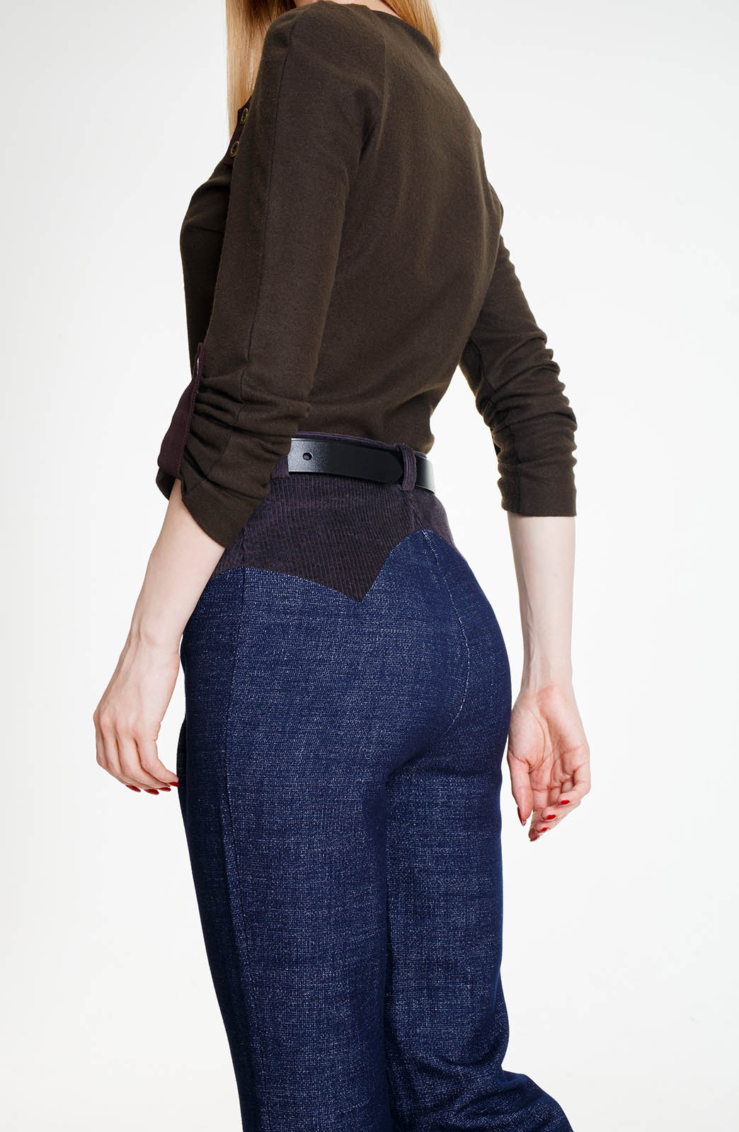 A three-quarter rear view highlighting the fit of the blue wool denim trousers. The dark corduroy yoke wraps around the waist, meeting the blue textured wool in a sharp, western-inspired pointed seam.
