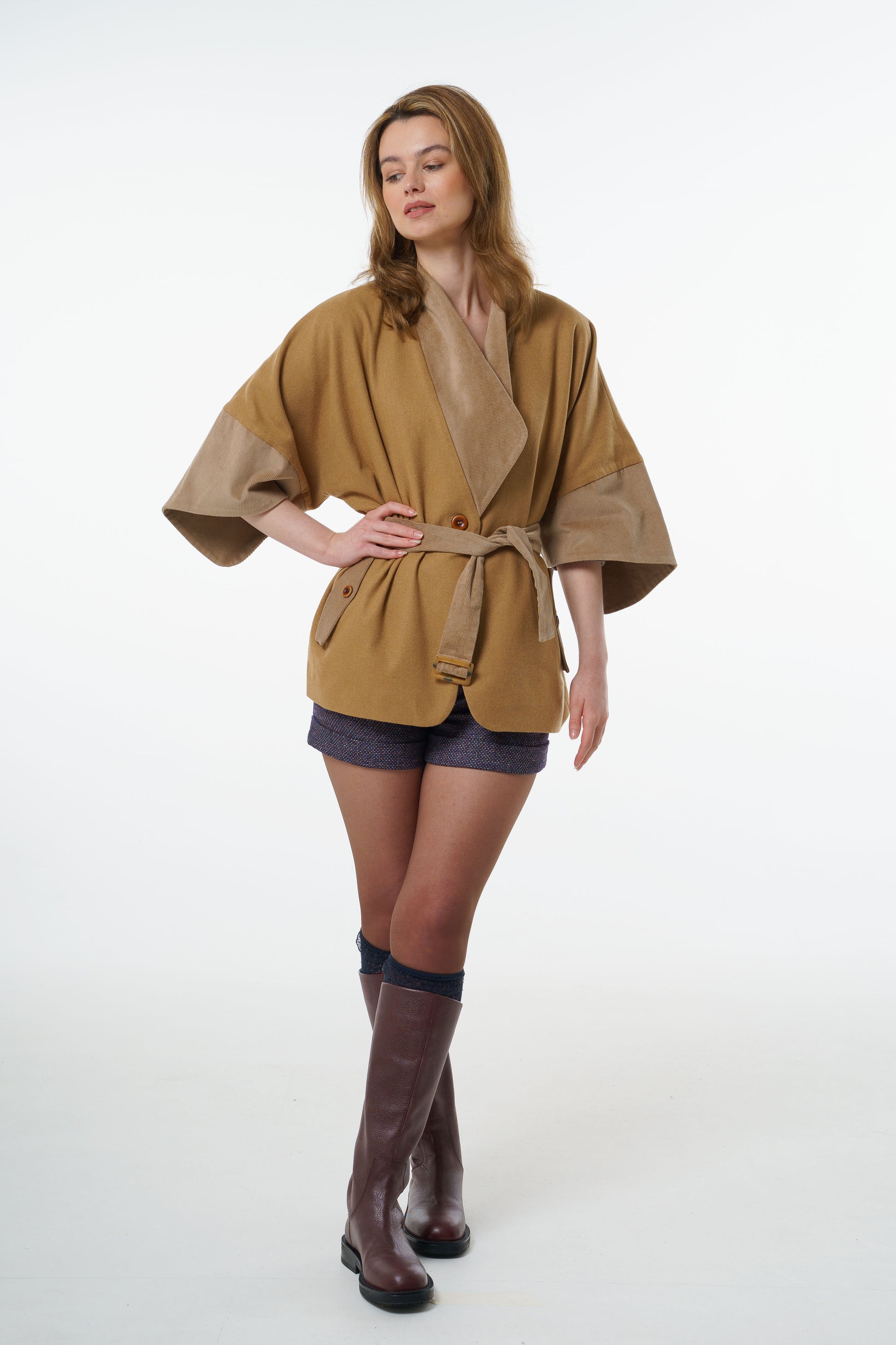Designer wool-cotton belted jacket with corduroy trims, styled with tweed shorts and tall leather boots, worn by a model.