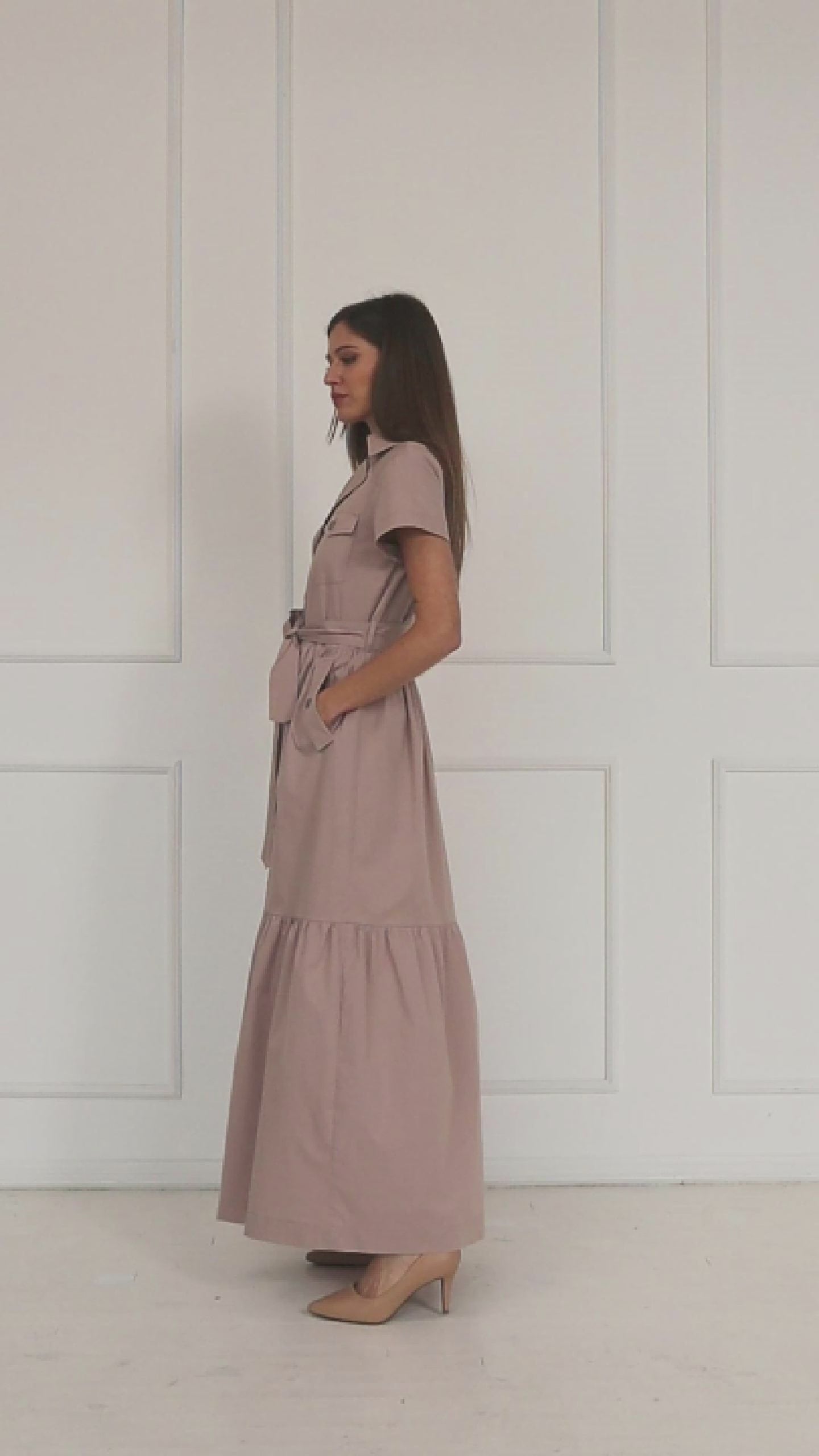 A studio video showing a model wearing the dusty mauve cotton button‑down maxi shirt-dress, highlighting the belted waist, tiered skirt, and the soft drape of the lightweight cotton.