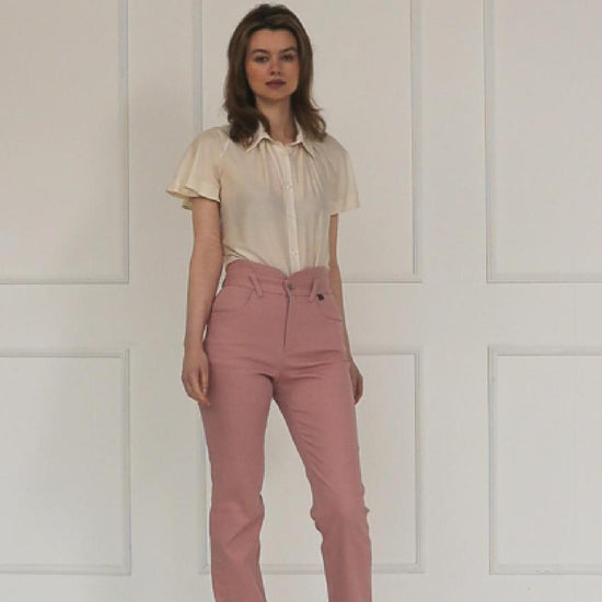 A studio video showing the rose‑dust high‑waisted stretch denim trousers, highlighting the layered waistband, tailored straight‑leg cut, and soft pastel finish.