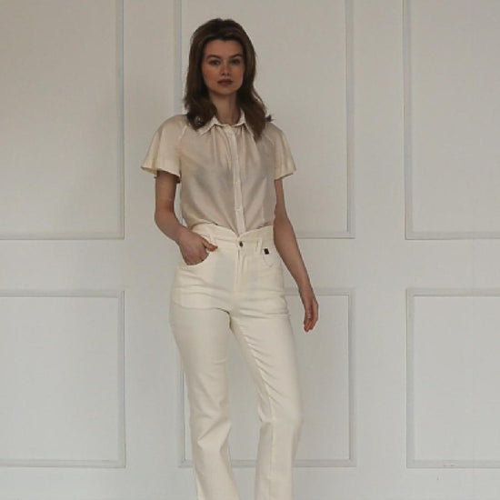 A studio video showing the cream high‑waisted stretch denim trousers, highlighting the layered waistband, tailored straight‑leg cut, and clean pastel finish.
