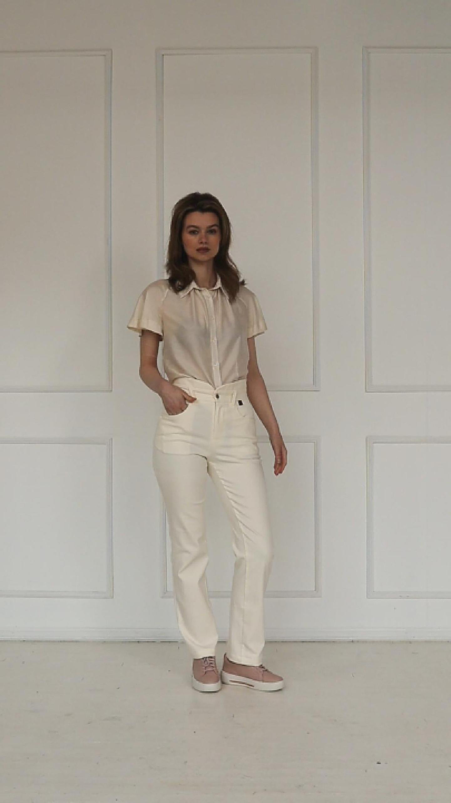 A studio video showing the cream high‑waisted stretch denim trousers, highlighting the layered waistband, tailored straight‑leg cut, and clean pastel finish.