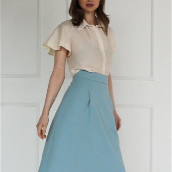A studio video showing the light blue high‑waisted A‑line midi skirt in a virgin wool blend, highlighting the structured pleat, clean flare, and tailored drape.