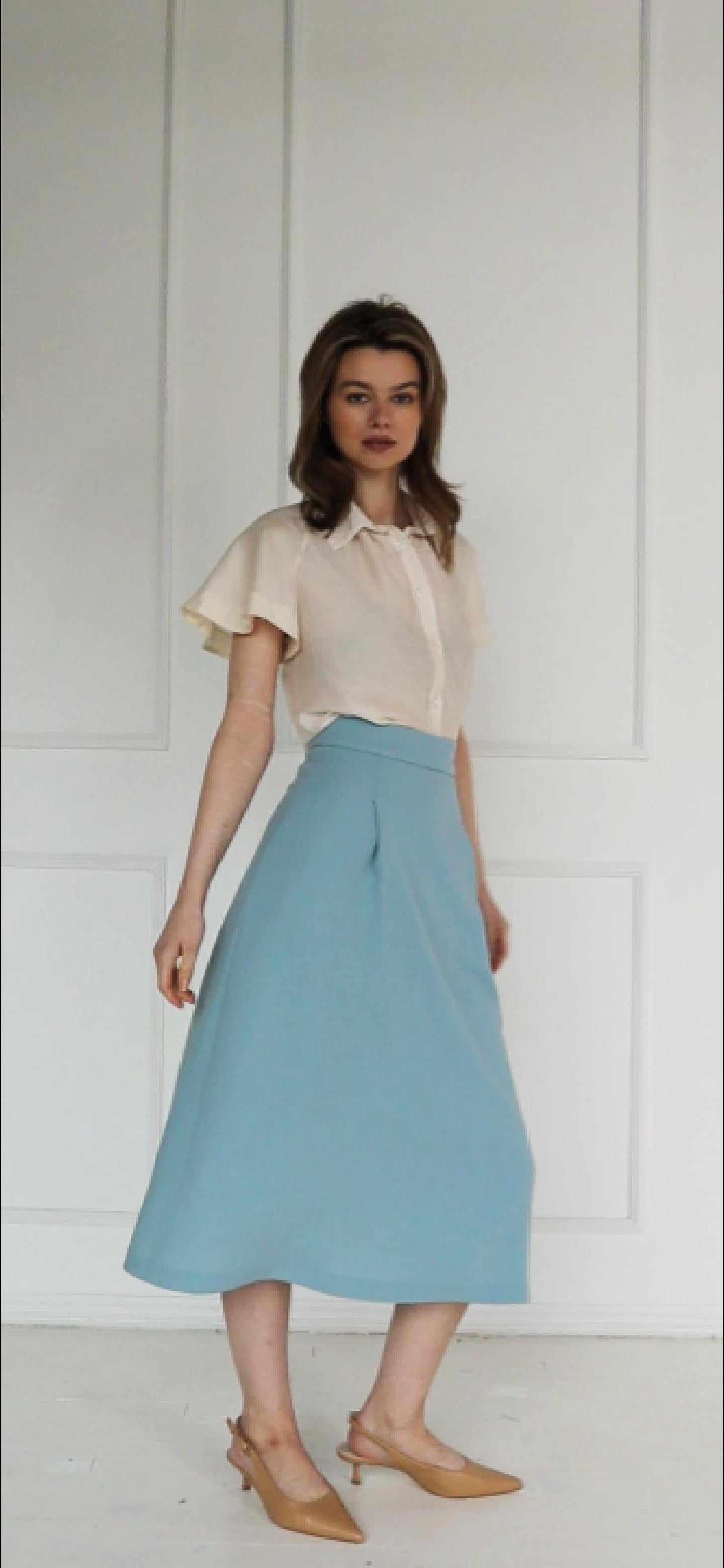 A studio video showing the light blue high‑waisted A‑line midi skirt in a virgin wool blend, highlighting the structured pleat, clean flare, and tailored drape.