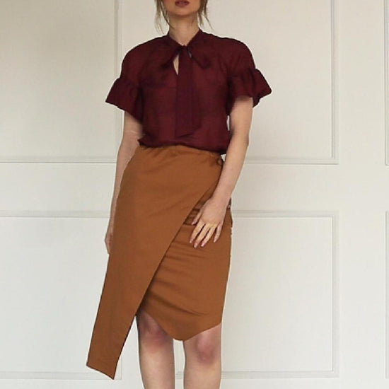 A studio video showing a camel wrap pencil skirt, highlighting the asymmetric overlay, side tie, and a burgundy cotton–silk raglan‑sleeve blouse, wearing by a model, highlighting the neck tie, ruffled cuffs, and fluid drape of the fabric.